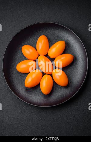 Tomates en forme de prune jaune vif et juteux sur un fond de béton texturé noir Banque D'Images