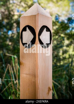 Portrait d'un marqueur de sentier de signalisation en bois avec deux flèches blanches sur fond noir à une intersection de sentier de randonnée dans la nature de Majorque. Banque D'Images