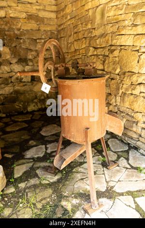 Machine de broyage de raisin ancienne et rouillée debout sur un sol en pierre dans un bâtiment avec des murs en pierre, concept de vinification Banque D'Images