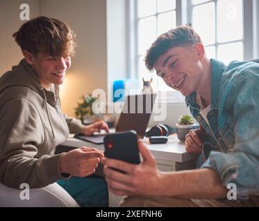 Deux garçons adolescents à la maison dans la chambre à coucher regardant message ou médias sociaux sur téléphone portable et rire Banque D'Images