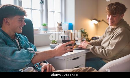 Deux garçons adolescents à la maison dans la chambre à coucher regardant message ou médias sociaux sur téléphone portable et rire Banque D'Images