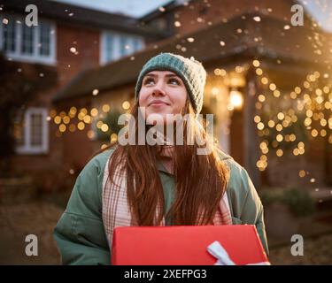 Fille adolescente souriante à l'extérieur habillée pour l'hiver dans la neige livrant des cadeaux de Noël Banque D'Images