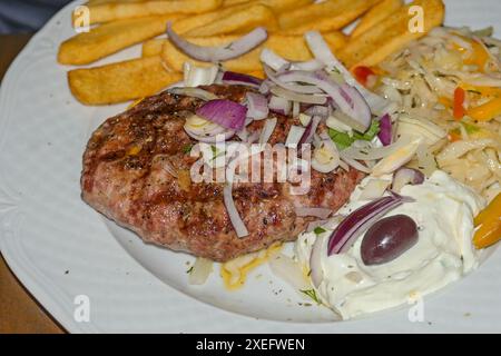 Bifteki grillé - boulettes de viande grecques avec frites, salade et tzatziki, garnies d'oignons crus, plat typique du restaurant grec ou gril de restauration rapide Banque D'Images