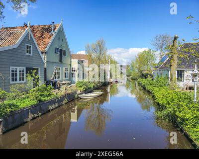 Un canal hollandais avec des maisons en bois une campagne luxuriante et verdoyante avec un feuillage vibrant et des collines ondulantes sous un ciel bleu clair Banque D'Images