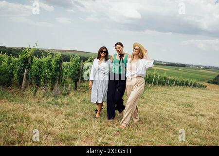 Trois jeunes femmes s'embrassent et marchent sur le vignoble. Banque D'Images