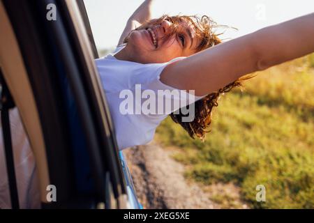 La jeune femme se penche par la fenêtre de la voiture et rit. Smiling Girl voyage et s'amuse sur la route Banque D'Images