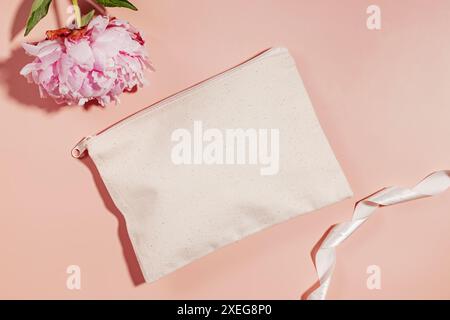 Maquette de sac cosmétique en toile et pivoine rose sur fond rose pastel, vue de dessus Banque D'Images
