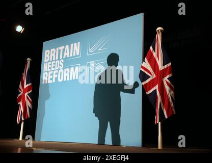 Boston, Angleterre, Royaume-Uni. 27 juin 2024. L'ombre du chef du parti NIGEL FARAGE est projetée sur la toile de fond du Parti réformiste britannique qui affiche le slogan du parti˜la Grande-Bretagne a besoin de réforme' alors qu'il parle devant une salle bondée et les encourage à voter pour le Parti réformiste britannique. Alors que le chef du parti NIGEL FARAGE rejoint le président du parti RICHARD TICE sur la piste de campagne pour parler du contrat du parti avec le peuple devant un public bondé au Hubberts Bridge Community Centre à Boston, Lincolnshire. La circonscription de Boston et Skegness a obtenu le plus grand vote de Leave du pays avec 75% au référendum sur l'UE et RICHARD TIC Banque D'Images