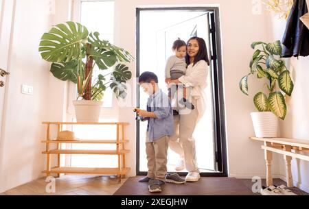 Une famille asiatique heureuse. Une jeune femme attirante aide à enlever les chaussures de sa petite fille Banque D'Images