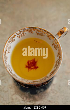 thé au safran jaune avec des fils rouges dans une tasse d'or ornée et blanche sur un plateau argenté Banque D'Images