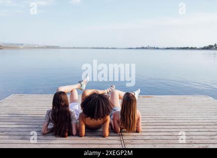 Les adolescentes multiraciales drôles se trouvent sur un plancher en bois à l'extérieur. Banque D'Images