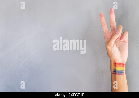 Main montrant le signe de paix avec le drapeau arc-en-ciel peint au poignet, exprimant la fierté LGBTQ+ Banque D'Images