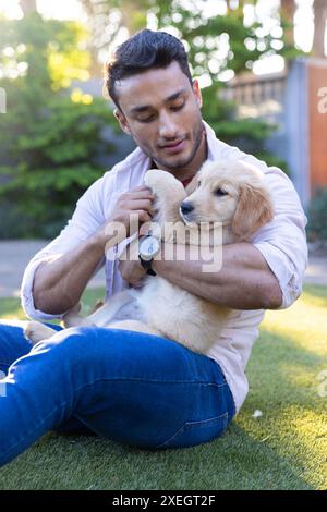 Homme assis sur l'herbe, câlin et jouant avec Golden retriever chiot Banque D'Images