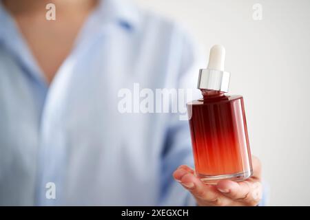 Les mains féminines dans une chemise bleue tiennent une bouteille rose de sérum. Banque D'Images