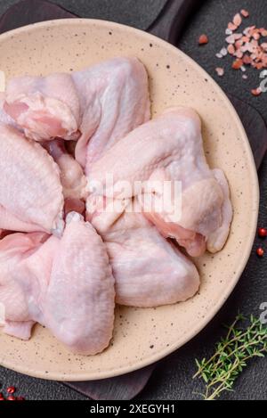 Ailes de poulet crues fraîches avec du sel et des épices préparées pour la cuisson sur un fond de béton foncé Banque D'Images