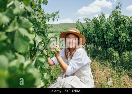 La jeune belle femme s'occupe du vignoble. Jolie fille caucasienne en robe de soleil beige, Banque D'Images