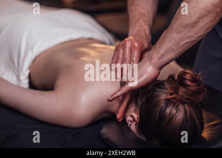 Heureuse jeune fille caucasienne obtenant le massage de retour dans le salon de spa. Mains soignées de masseuse masculine Banque D'Images