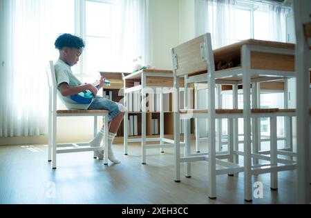 Petit artiste jouant du ukulélé au fond de la salle de classe, en attendant que des amis entrent dans la salle de classe Banque D'Images