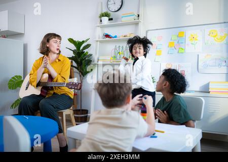 En classe, le professeur et les élèves chantent ensemble, et les garçons dansent joyeusement. Banque D'Images