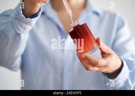 Les mains féminines dans une chemise bleue tiennent une bouteille rose de sérum. Banque D'Images