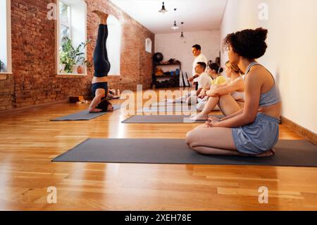 L'entraîneur montre la tribune à ses élèves. Un groupe de personnes de différents âges et ethnies font du yoga dans un club de fitness. Yo Banque D'Images