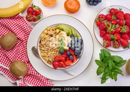 Granola avec fraises, kiwi, banane et bleuets dans une assiette ronde sur une table blanche. Banque D'Images