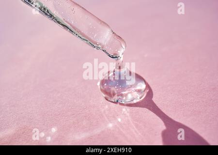 Pipette avec sérum scintillant au soleil sur fond rose. Banque D'Images