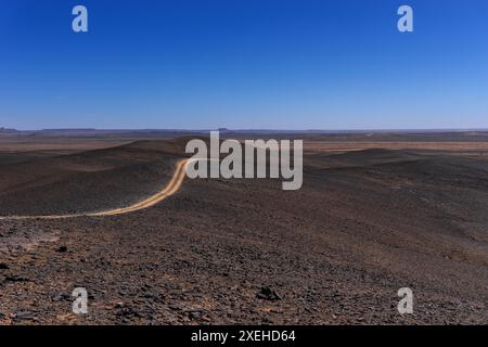 Vue sur un chemin de terre menant à travers le désert de roche et de sable du sud-est du Maroc Mear Merzouga et Erg Chebbi Banque D'Images