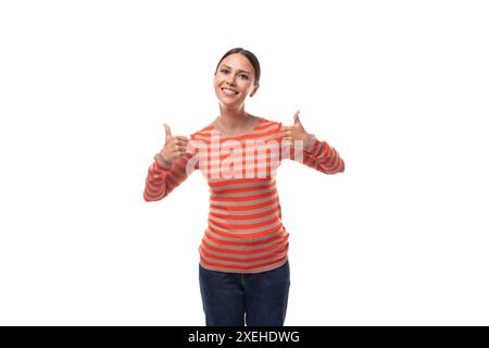 Jeune femme brune slim élégante vêtue d'un chemisier orange rayé et d'un Jean sur un fond blanc Banque D'Images