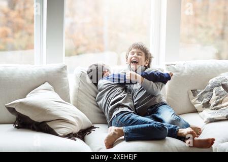 Garçons, enfants et jeu de chatouillement sur le canapé, rire et blague drôle pour les liens frères et sœurs à la maison. Enfants, frères et bonheur dans le salon pour la comédie Banque D'Images