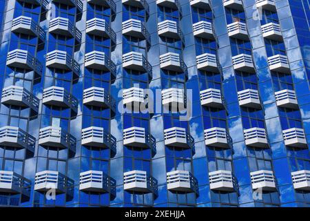 Façade de bâtiment en verre moderne avec un motif abstrait de balcons répétitifs, reflétant le ciel et les nuages. Banque D'Images