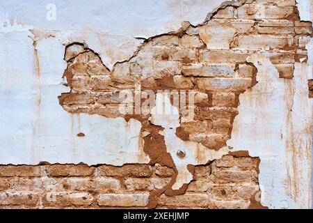 Gros plan d'un mur qui se détériore montrant des couches de vieille peinture qui s'écaillent pour révéler des briques en dessous, représentant la pourriture et le passage du temps. Banque D'Images