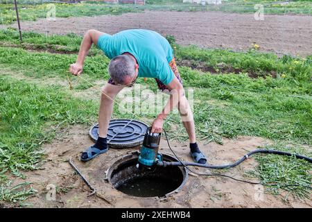 Man abaisse la pompe de drainage submersible haute pression dans la fosse septique pour pomper les eaux usées et les jeter. Banque D'Images