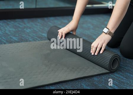 Femme de fitness pliant tapis d'exercice avant de travailler dans le studio de yoga. Tapis de yoga roulant après la formation à un mode de vie sain Banque D'Images