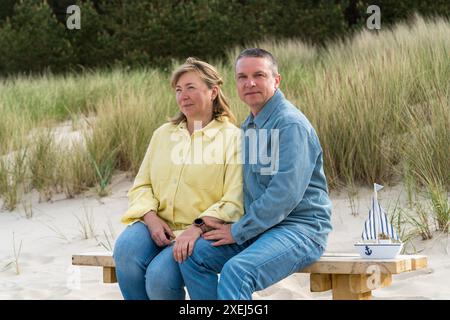 Un couple d'âge moyen en vacances à la mer. Un homme et une femme profitent de leurs vacances. Ils sont assis sur un banc sur la mer Baltique, avec des dunes en backgr Banque D'Images