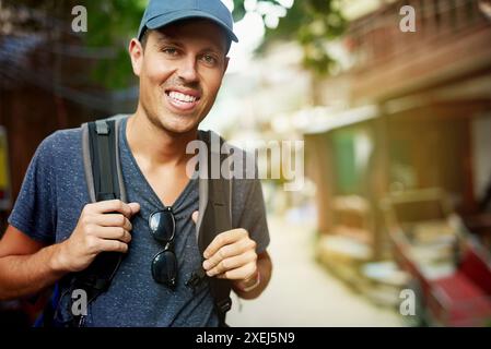 Voyage, portrait et homme sac à dos en Thaïlande pour l'aventure, les vacances ou le tourisme par maisons de bambou. Touriste ou voyageur dans la rue à l'expérience Banque D'Images