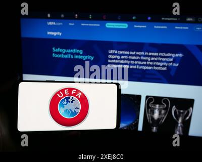 Personne tenant un smartphone avec le logo de l'Union des associations européennes de football (UEFA) devant le site. Concentrez-vous sur l'affichage du téléphone. Banque D'Images