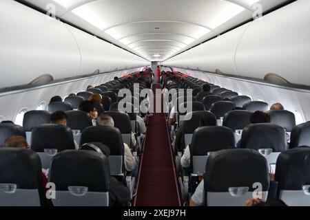 Cabine d'avion commercial à couloir unique avec rangées de sièges, avec un équipage de cabine féminin dans le couloir. Classe économique entièrement occupée. Tir symétrique. Banque D'Images