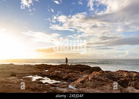 Femme marchant sur la rive rocheuse au coucher du soleil à Hawaï. Banque D'Images