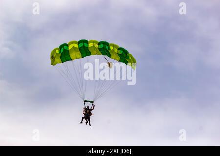 Parachutistes tandem avec un parachute vert descendant dans un ciel nuageux. Banque D'Images