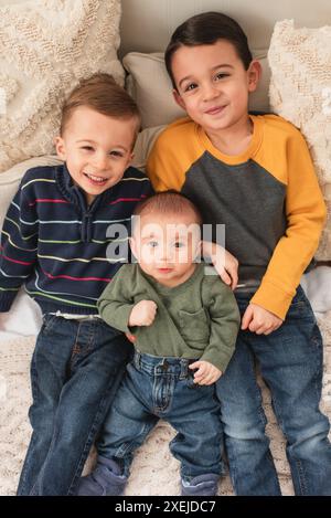 Trois frères souriants couchés dans le lit sur des oreillers et des couvertures confortables Banque D'Images