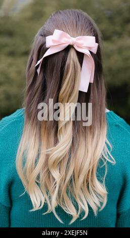 Femme aux cheveux longs noués avec un noeud rose, portant une sueur verte Banque D'Images