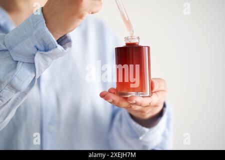 Les mains féminines dans une chemise bleue tiennent une bouteille rose de sérum. Banque D'Images