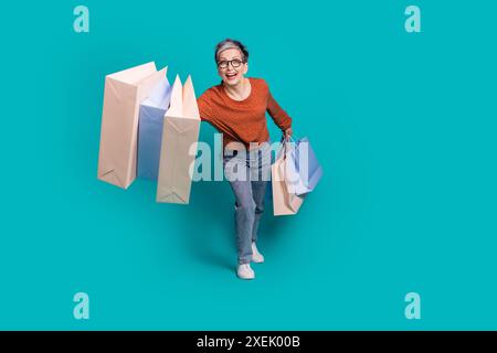 Photo pleine taille de jolis sacs à provisions féminins retraités portant une tenue marron tendance isolée sur fond de couleur aigue-marine Banque D'Images