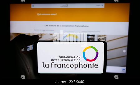 Personne tenant un téléphone portable avec le logo de l'Organisation internationale de la Francophonie devant la page Web. Concentrez-vous sur l'affichage du téléphone. Banque D'Images