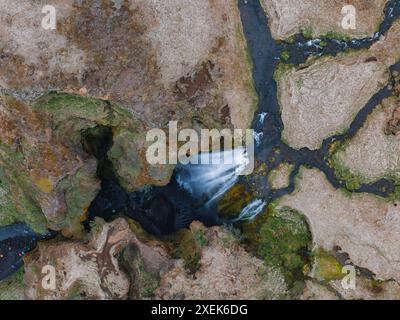 Vue aérienne de la majestueuse cascade et de la rivière sinueuse dans le terrain rocheux d'Islande Banque D'Images