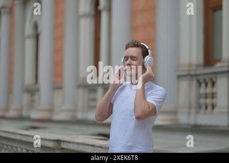 Un jeune homme avec une tablette dans les mains écoutant de la musique avec des écouteurs dans une rue de Vienne. Concept de style de vie de détente et de plaisir. Banque D'Images