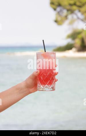 Femme tenant un verre plein d'une boisson rouge rafraîchissante contre la mer bleue, Cold-Brew Iced Sweet Hibiscus Tea, boisson rafraîchissante d'été, détox, régime et santé Banque D'Images