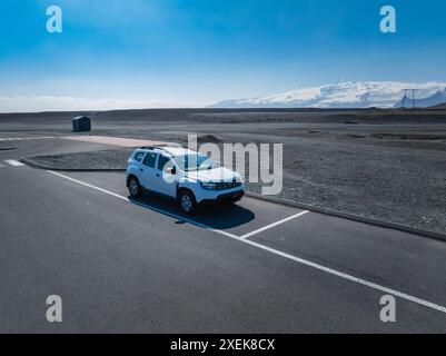 SUV blanc sur route pavée dans le paysage de gravier gris foncé désolé, Islande Banque D'Images