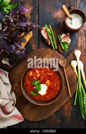 Borscht ukrainien. Soupe de racines de betterave rouge avec crème, herbes, assaisonnements et épices servie avec morceau de pain de seigle et poitrine séchée et oignons sur bois R Banque D'Images